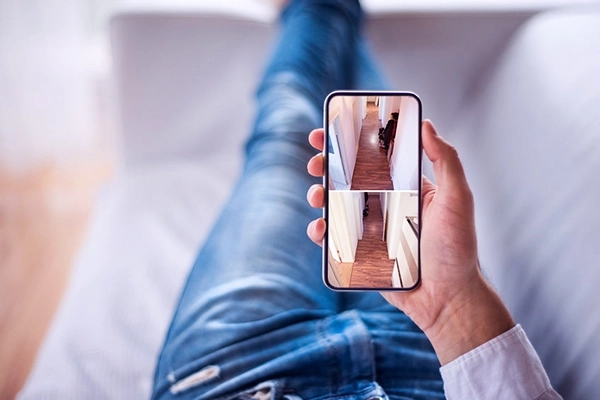 Person auf einem Sofa mit einem Smartphone, das ihr Haus steuert